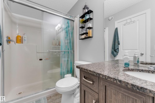 Bathroom featuring a glass-enclosed shower with a built-in shelf, a toilet, and a vanity with a stone-look countertop and an integrated sink - 1750 27 Street, Edmonton, AB 