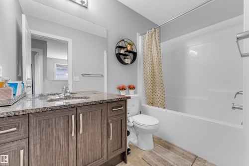 Bathroom featuring a wood-finish vanity with a stone-look countertop, a built-in sink, and a large wall-mounted mirror - 1750 27 Street, Edmonton, AB 