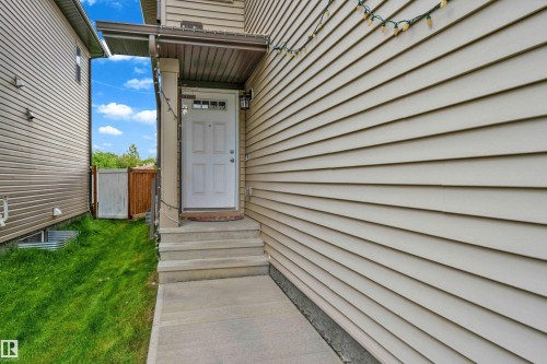 Side entrance featuring a solid white door with upper lites, covered porch, concrete steps, and a concrete walkway - 1750 27 Street, Edmonton, AB 