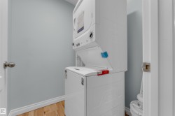 Dedicated laundry area featuring a stacked washer and dryer unit, wood-finish flooring, and light blue walls with white trim - 