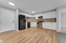 Kitchen featuring wood-finish flooring, white cabinetry, a neutral tile backsplash, stainless steel appliances, and a black refrigerator - 326 111 Edwards Drive, Edmonton, AB 