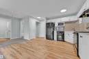 Open-concept kitchen with wood-finish flooring, white cabinetry, and black appliances - 326 111 Edwards Drive, Edmonton, AB 