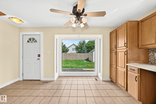 Tile flooring, full-light door with decorative glass, wood-finish cabinetry, light-toned countertops, and a ceiling fan with integrated lighting - 18636 71 Avenue, Edmonton, AB 
