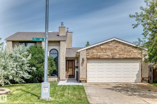 Residential exterior featuring a stone-clad garage gable, an arched window, a paneled garage door, a concrete driveway, and a shingle roof - 18636 71 Avenue, Edmonton, AB 