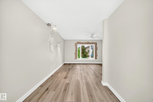 Expansive room featuring wide plank wood-finish flooring, a contemporary wall-mounted light fixture, crisp white baseboards, and a ceiling fan - 18636 71 Avenue, Edmonton, AB 