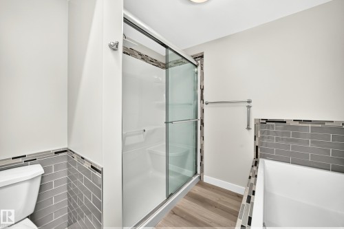 Bathroom featuring a glass-enclosed shower with integrated seating, subway tile wall accents, a built-in tub, and wood-finish flooring - 18636 71 Avenue, Edmonton, AB 
