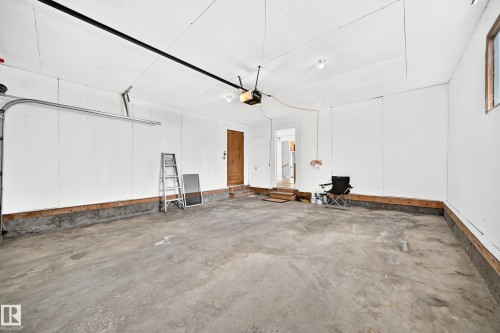 Spacious garage featuring a concrete floor, white walls, exposed wood framing at the base, and a single window for natural light - 18636 71 Avenue, Edmonton, AB 
