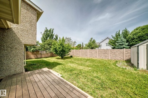 Expansive backyard featuring a wood deck, a manicured lawn, a concrete block privacy fence, mature trees, and a storage shed - 18636 71 Avenue, Edmonton, AB 