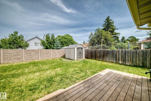 Expansive green lawn featuring a wooden deck, a storage shed, and a stone-look fence - 18636 71 Avenue, Edmonton, AB 