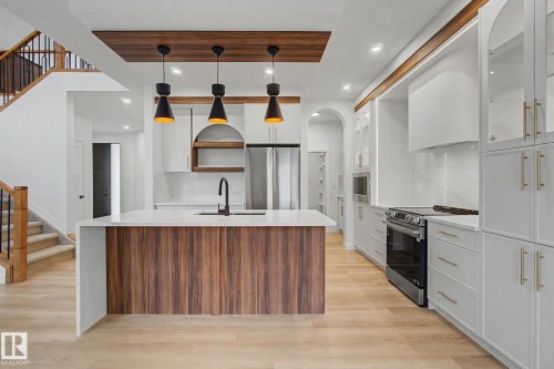 Contemporary kitchen featuring an island with wood-finish paneling and a light-toned countertop, integrated sink with a matte black faucet, and three pendant lights suspended from a wood-finish ceiling accent - 4 Willow Heights Drive, Stony Plain, AB 
