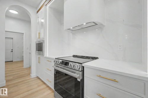 Modern kitchen featuring a stainless steel range, built-in microwave, white shaker cabinetry with gold-tone hardware, white countertops, and a full-height backsplash - 4 Willow Heights Drive, Stony Plain, AB 