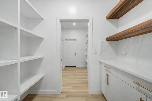 Dedicated pantry space featuring white shelving, light wood-finish flooring, white cabinetry with brass hardware, a white countertop, and wood-finish floating shelves - 4 Willow Heights Drive, Stony Plain, AB 