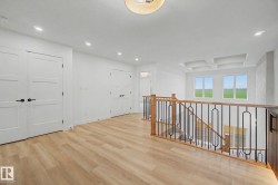 Upper-level landing featuring wood-finish flooring, white paneled doors, recessed lighting, a coffered ceiling detail, and a staircase with a wooden handrail and black metal balusters - 