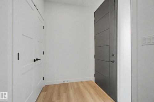 Entryway featuring a modern gray door with horizontal paneling, light wood-finish flooring, and white paneled doors with black hardware - 4 Willow Heights Drive, Stony Plain, AB 