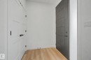 Entryway featuring a modern gray door with horizontal paneling, light wood-finish flooring, and white paneled doors with black hardware - 4 Willow Heights Drive, Stony Plain, AB 