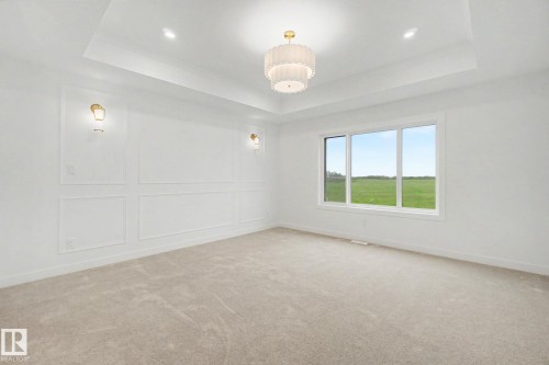 Spacious room featuring a tray ceiling with a central chandelier, decorative wall paneling, and wall sconces - 4 Willow Heights Drive, Stony Plain, AB 