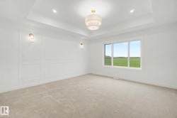 Spacious room featuring a tray ceiling with a central chandelier, decorative wall paneling, and wall sconces - 