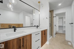 Dual vanity with integrated sinks, white countertops, wood-finish cabinetry, matte black fixtures, and a glass-enclosed shower - 