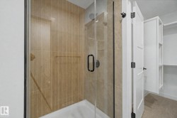 Glass-enclosed shower with wood-finish tile surround and a matte black shower head - 