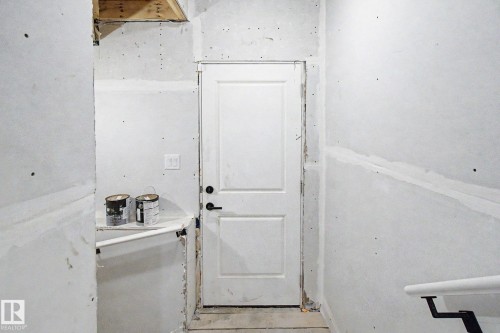 Interior space featuring a white two-panel door with black hardware, unfinished drywall, exposed ceiling joists, and a partial white handrail - 4 Willow Heights Drive, Stony Plain, AB 