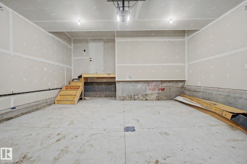Spacious garage featuring a concrete floor, unpainted drywall, two ceiling-mounted light fixtures, and a wooden stairwell with a landing and white door - 4 Willow Heights Drive, Stony Plain, AB 