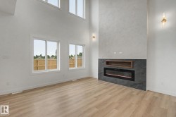 Spacious interior featuring soaring ceilings, a striking electric fireplace with a dark tile surround, a built-in wood-finish media niche, and tall windows providing abundant natural light - 