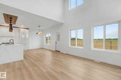 Spacious open-concept living area featuring high ceilings, wood-finish flooring, and multiple large windows - 