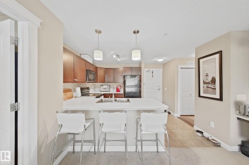 Kitchen featuring an eat-at peninsula, wood-finish cabinetry, stainless steel appliances, and pendant lighting - 117 3715 Whitelaw Lane, Edmonton, AB 