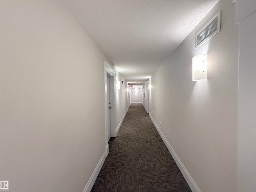 Hallway featuring neutral wall paint, wall-mounted sconce lighting, and textured carpet flooring - 117 3715 Whitelaw Lane, Edmonton, AB 
