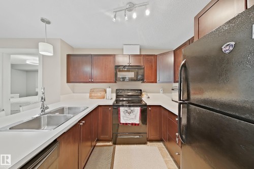 U-shaped kitchen featuring wood-finish cabinetry, light-toned countertops, and a double basin stainless steel sink with a chrome faucet - 117 3715 Whitelaw Lane, Edmonton, AB 