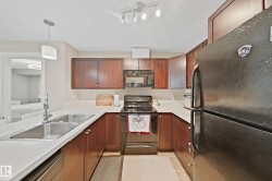 U-shaped kitchen featuring wood-finish cabinetry, light-toned countertops, and a double basin stainless steel sink with a chrome faucet - 