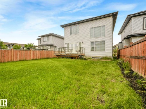 Expansive fenced backyard with a wooden deck featuring glass panel railings, white siding, and prominent windows - 6607 53 Avenue, Beaumont, AB 