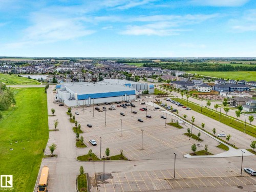 Large commercial building with extensive paved parking, surrounded by green spaces and a residential development - 6607 53 Avenue, Beaumont, AB 