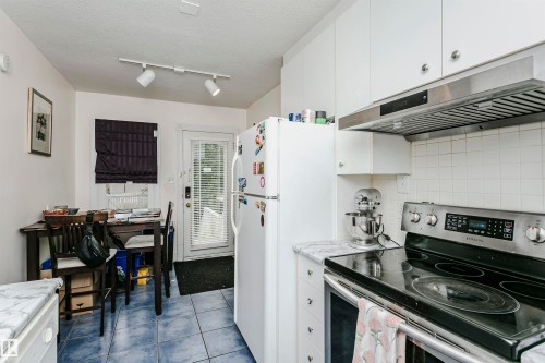 Kitchen featuring white cabinetry, a stainless steel electric range with an overhead vent hood, and marble-finish countertops - 11105 81 Avenue, Edmonton, AB 