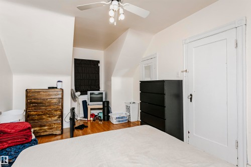 Bedroom featuring wood-finish flooring, a ceiling fan with integrated lighting, and a white paneled door with decorative trim - 11105 81 Avenue, Edmonton, AB 