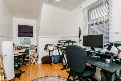 Hardwood flooring and sloped ceilings define this versatile room, featuring two windows with blinds, and white trim - 11105 81 Avenue, Edmonton, AB 