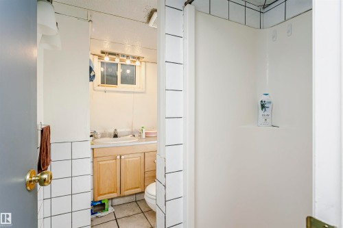Bathroom featuring a built-in shower stall with white tile surround, a single vanity with wood cabinetry, and a window for natural light - 11105 81 Avenue, Edmonton, AB 