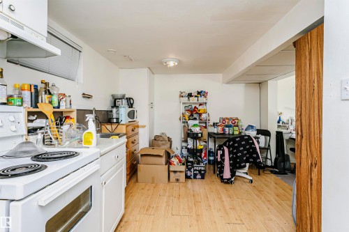 Kitchen area featuring a white electric range with an overhead vent hood, white cabinetry, and a stainless steel sink with a window above - 11105 81 Avenue, Edmonton, AB 