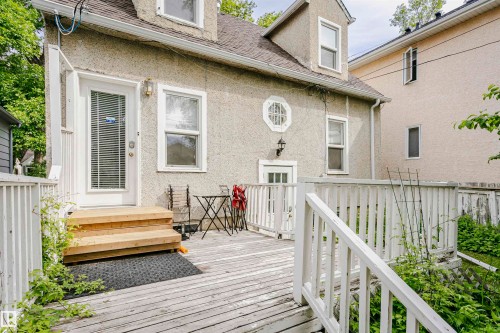 Rear exterior featuring a stucco facade, multiple windows, a white door with integrated blinds, and a white wooden deck with railing - 11105 81 Avenue, Edmonton, AB 
