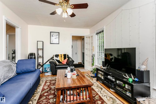 Living area featuring wood-finish flooring, a ceiling fan with integrated lighting, and white paneled walls - 11105 81 Avenue, Edmonton, AB 