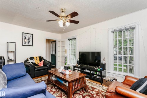 Living area featuring a ceiling fan with integrated lighting, wood-finish flooring, and large multi-pane windows - 11105 81 Avenue, Edmonton, AB 
