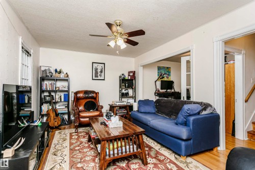 Living area featuring wood-finish flooring, a ceiling fan with integrated lighting, and crown molding - 11105 81 Avenue, Edmonton, AB 
