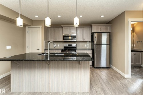 Modern kitchen featuring a large island with a dark countertop, stainless steel appliances, light wood-finish cabinetry, and wood-finish flooring - 2397 Glenridding Boulevard, Edmonton, AB 