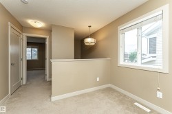 Carpeted upper-level landing featuring a large window, a semi-flush mount light fixture, a modern drum pendant light, and a white railing - 