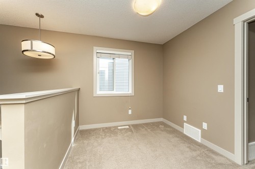 Carpeted interior space featuring a single window with blinds, a drum pendant light fixture, a flush mount ceiling light, and neutral wall paint - 2397 Glenridding Boulevard, Edmonton, AB 