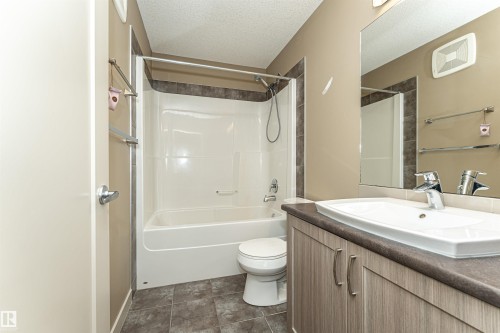 Bathroom featuring a white bathtub and shower combination with dark tile surround, a single vanity with a white basin sink, wood-finish cabinetry, and a large wall-mounted mirror - 2397 Glenridding Boulevard, Edmonton, AB 