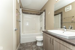 Bathroom featuring a white bathtub and shower combination with dark tile surround, a single vanity with a white basin sink, wood-finish cabinetry, and a large wall-mounted mirror - 