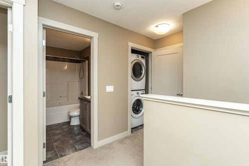 Upper-level laundry closet featuring a stacked washer and dryer, complemented by a nearby bathroom with a tub/shower combination, dark wood-finish vanity, and tile flooring - 2397 Glenridding Boulevard, Edmonton, AB 