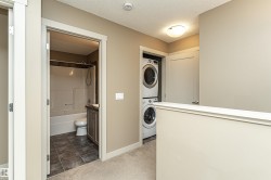 Upper-level laundry closet featuring a stacked washer and dryer, complemented by a nearby bathroom with a tub/shower combination, dark wood-finish vanity, and tile flooring - 