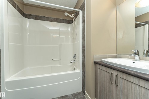 Bathroom featuring a white tub and shower combination with dark tile surround - 2397 Glenridding Boulevard, Edmonton, AB 